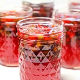 Jars filled with red plum jelly preserves, featuring intricate patterned glass designs.