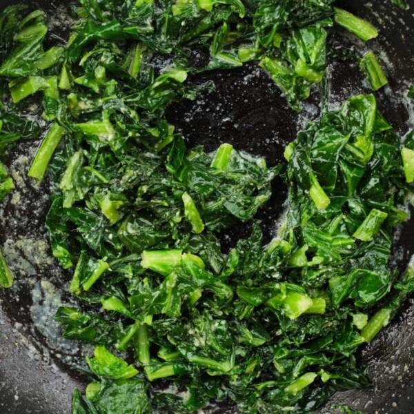 Sautéed collard greens in a black skillet with a light garlic sauce.