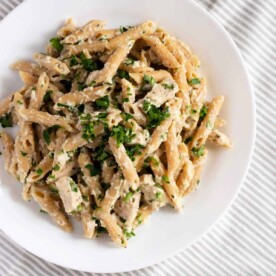 A plate of creamy Slow Cooker Chicken Alfredo, made with tender frozen chicken and fresh herbs, rests invitingly on a striped tablecloth.