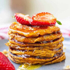 A stack of sweet potato pancakes topped with sliced strawberries and drizzled with syrup sits enticingly on a plate.