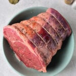 A bowl showcasing a seasoned raw beef roast with visible spices, ready for its transformation into a succulent dish. Accompanied by aromatic bay leaves and a pepper shaker, it sets the stage for those eager to discover how to cook a roast perfectly.