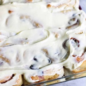 Sweet rolls adorned with frosty cinnamon goodness rest invitingly in a glass baking dish on a marble surface.