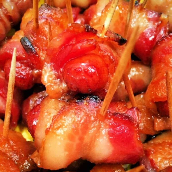 Close-up image of Bacon Wrapped Smokies secured with toothpicks. The bacon is cooked to a crispy, golden-brown finish in the Ninja Foodi. The appetizers are closely packed, showcasing the texture and color variation from the caramelized and well-cooked bacon.