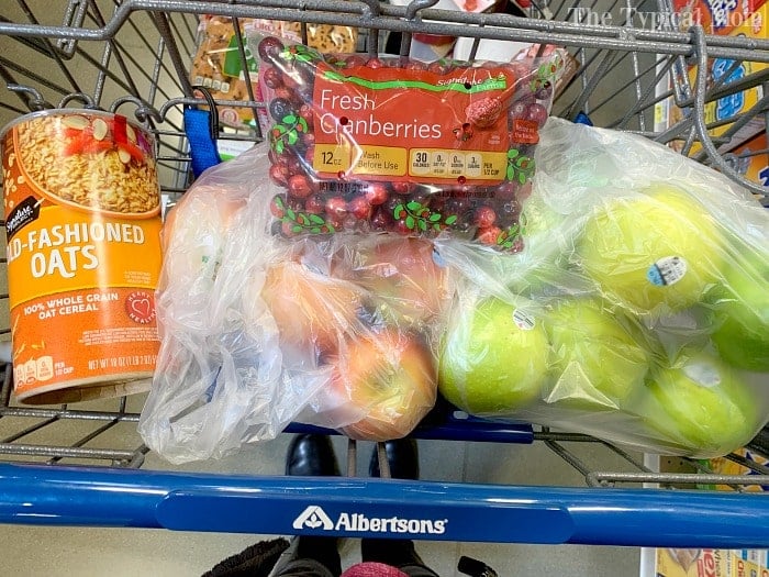 Shopping cart with oats, fresh cranberries ready for instant pot cranberry sauce, green apples, and onions in plastic bags at Albertsons.