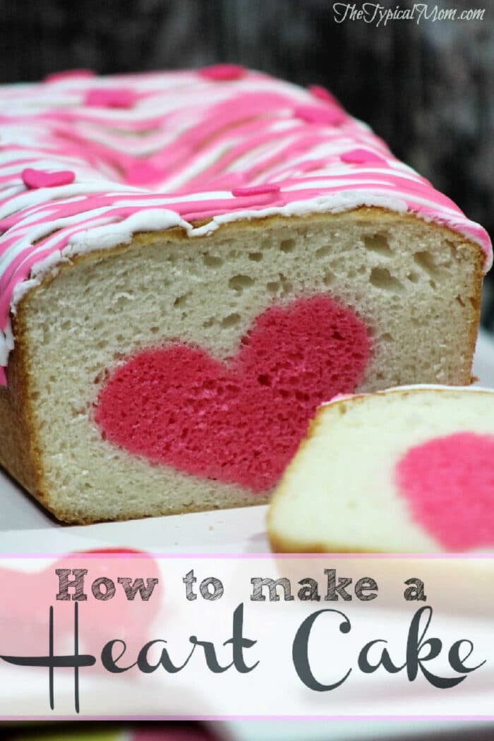 Surprise cake is fun with a hidden shape inside!! Easy video tutorial too showing you how to make one yourself. #surprisecake #cake #shape A surprise inside cake loaf with a pink heart shape in the center, topped with pink and white icing, and a sliced piece in front.