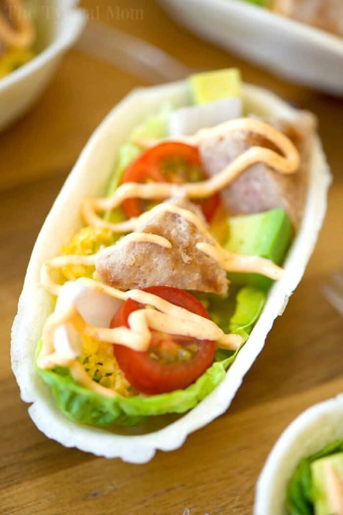 A taco bowl with lettuce, chicken, cherry tomatoes, cheese, avocado, and a drizzle of sauce—an irresistible choice for taco lovers or fans of turkey burger boats.