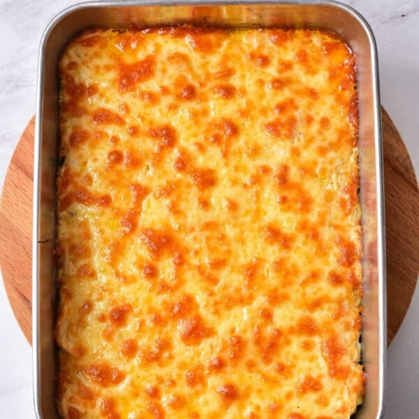 A baked cheesy casserole of savory delight, this Buffalo Chicken Dip rests invitingly in a rectangular metal dish atop a rustic wooden board.