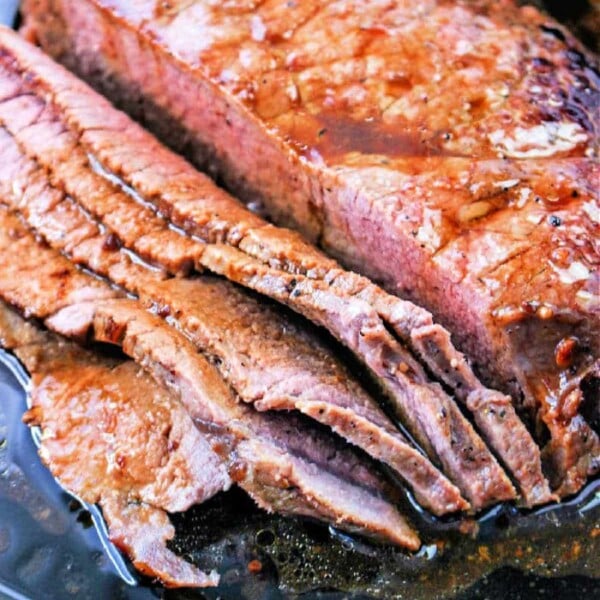 Sliced roasted flank steak nestled in a cast iron pan with flavorful juices.