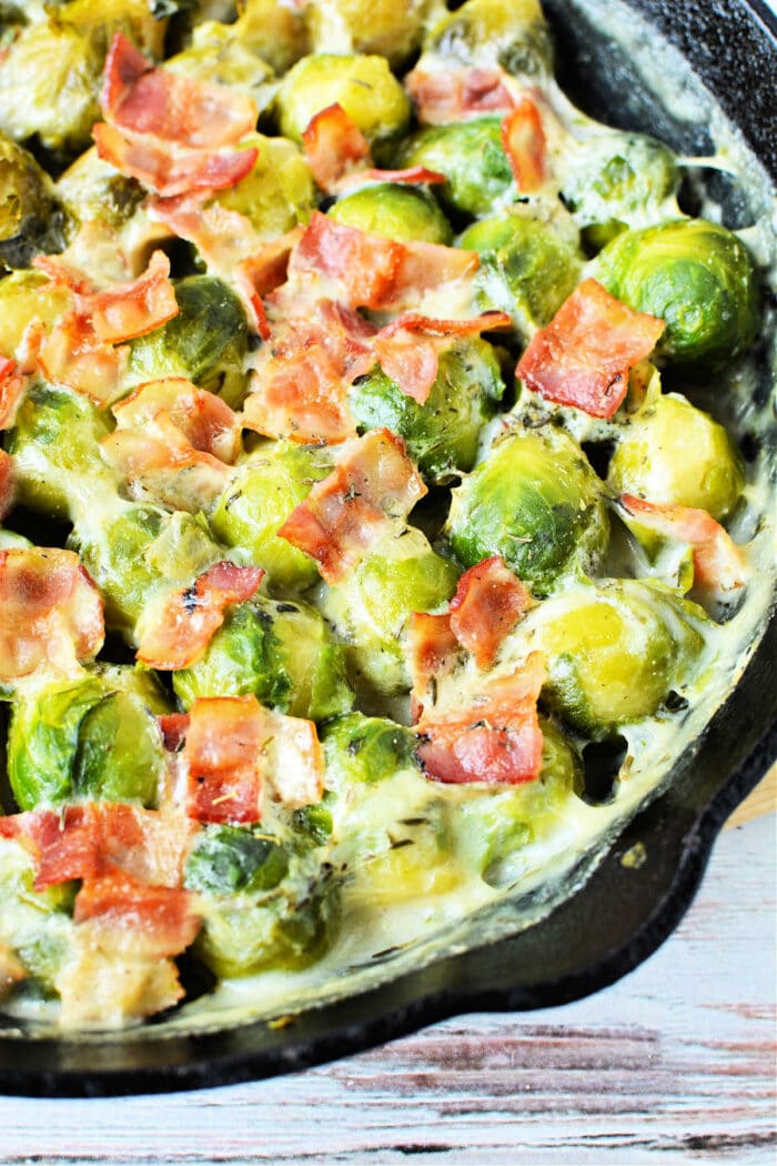 Creamy Brussels sprouts with cream and crispy bacon sizzle in a cast iron skillet.