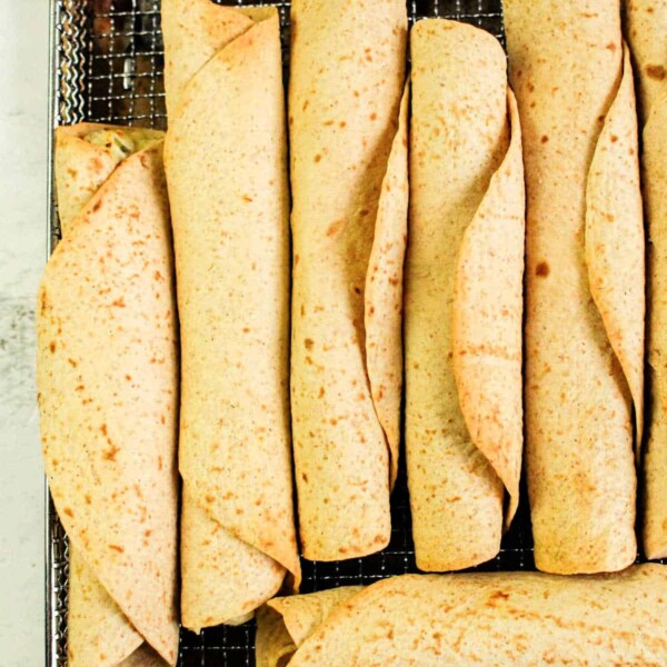 A tray of neatly arranged chicken taquitos rolled to perfection sits on a metal rack. The tortillas, cooked evenly in an air fryer, are light brown with visible specks. Beneath the tray lies a white, textured surface.