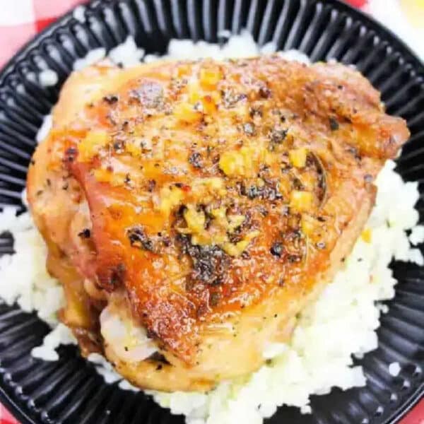 Roast chicken thigh with herbs served on a bed of white rice on a black plate—perfect inspiration if you’re wondering how long to bake bone-in chicken thighs at 350 for tender, flavorful results.