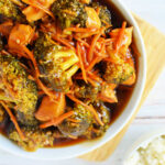 A bowl of Instant Pot Chicken and Broccoli stir-fry is perfectly complemented by carrots in a savory sauce, served with a side of rice.