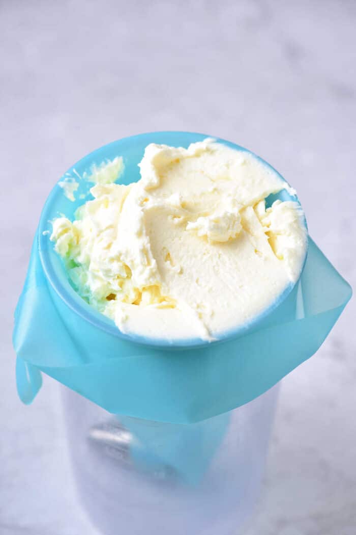 Homemade frosting in a blue churn with cream residue on top, resembling the rich texture of a Lemon Curd Cake, set against a light background.