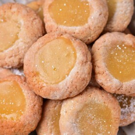 A plate of lemon curd cookies with a dollop of zesty curd in the center, dusted lightly with powdered sugar.