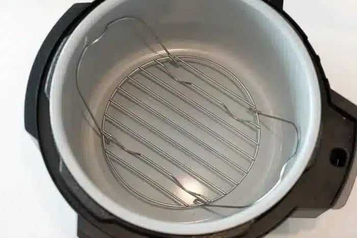 The image shows the interior of an empty electric pressure cooker, ready to prepare delicious meals like an air fryer whole chicken. The metal insert and cooking rack are visible, and the pot is clean with a stainless steel inner surface and a black exterior casing.