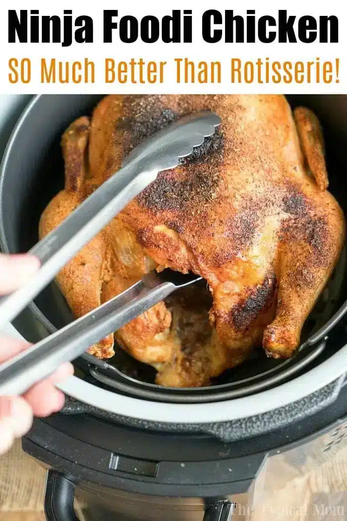 A whole roasted chicken is being lifted out of a Ninja Foodi cooker using metal tongs. The text above reads "Ninja Foodi Air Fryer Chicken: SO Much Better Than Rotisserie!