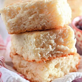 Two stacked fluffy butter swim biscuits, made from just 4 ingredients, rest on a white cloth with a blurred backdrop of jam.