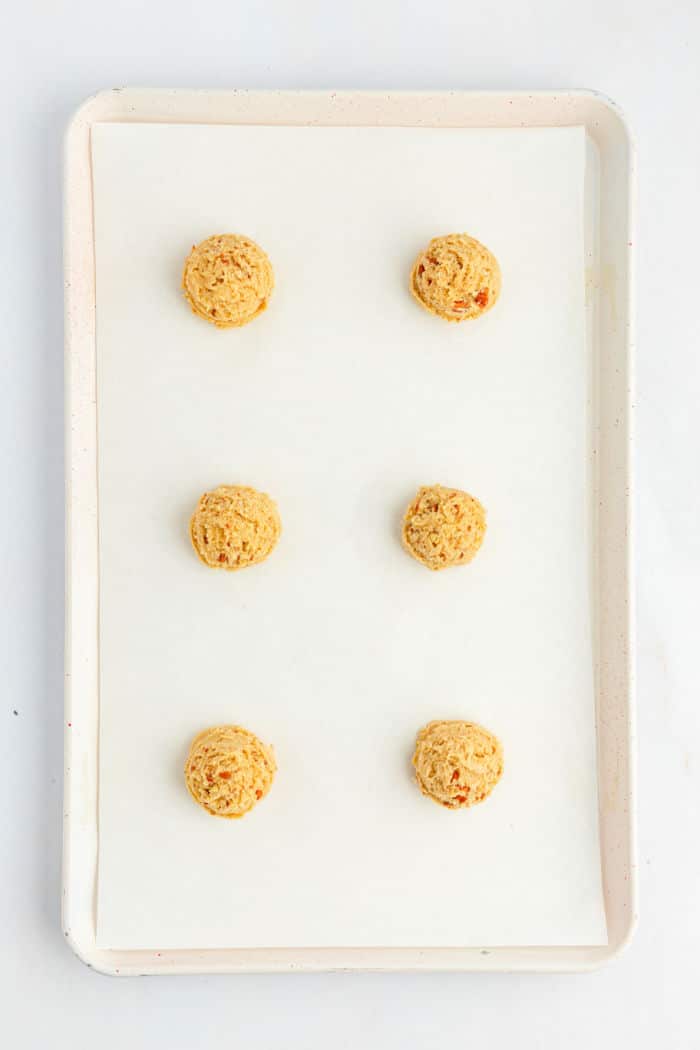 A white baking tray lined with parchment paper holds six evenly spaced raw Bear Paw Cookies dough balls arranged in two columns and three rows. The tray is shown from above against a white background.