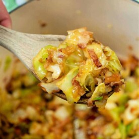 A wooden spoon lifts a delicious mixture, embodying the perfect cabbage and bacon recipe, right from the pot.