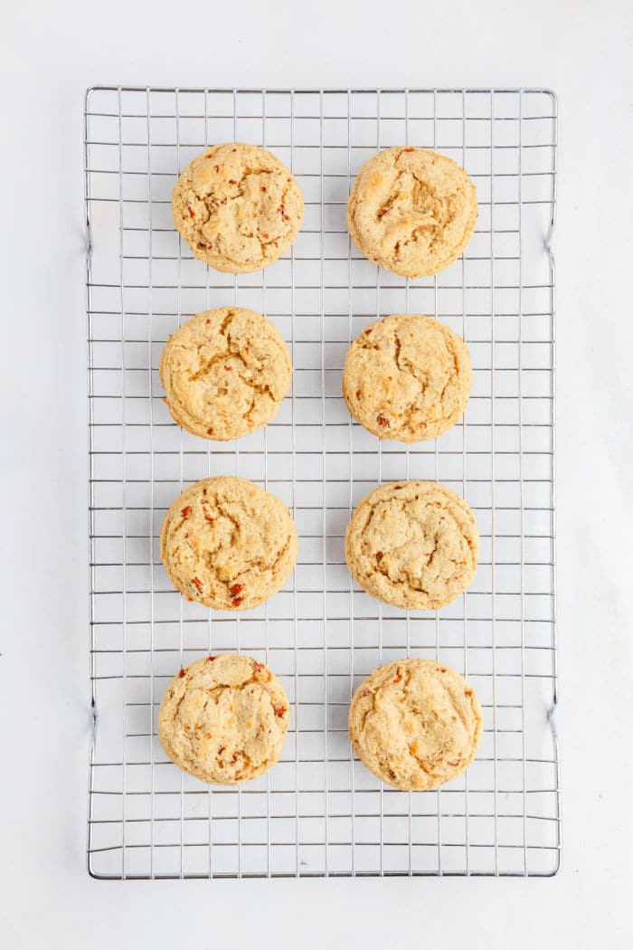 A cooling rack holds eight evenly spaced Bear Paw Cookies that are light golden brown with a crinkled texture, placed on a white background.