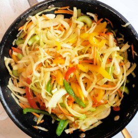 A skillet filled with sautéed mixed vegetables, featuring bell peppers, onions, and zucchini, takes inspiration from a Jamaican Cabbage Recipe.