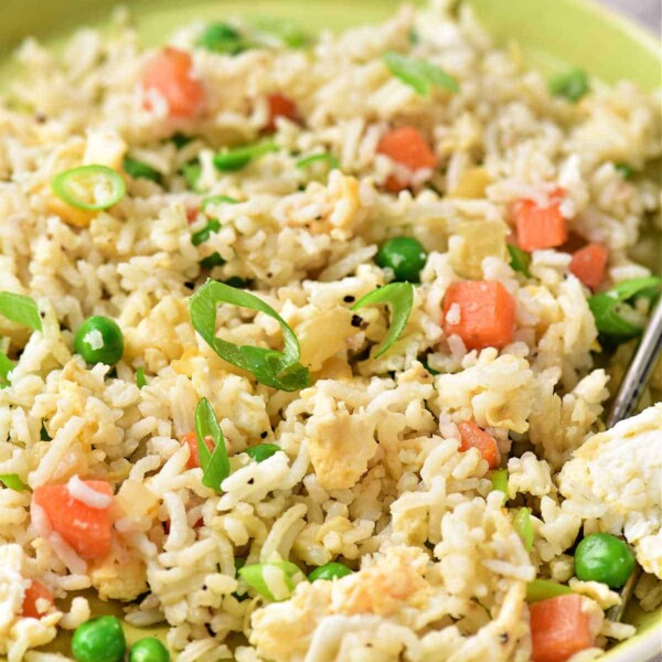 A plate of egg fried rice with peas, chopped tomatoes, and green onions showcases a delicious take on how to make egg fried rice at home.