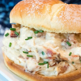 Enjoy a creamy chicken sandwich infused with rich cream cheese and chives, served on a bun atop a crisp white plate. This delightful creation draws inspiration from beloved crockpot chicken recipes, ensuring a comforting and savory meal experience.