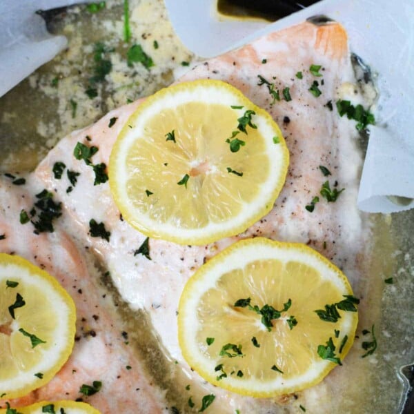 Crockpot salmon fillet topped with lemon slices and herbs on parchment paper.