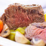 Close-up of a sliced Cross Rib Roast with tender carrots, potatoes, and mushrooms on a plate.