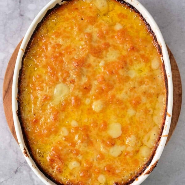 Dairy-free scalloped potatoes lie golden-brown in an oval casserole on a marble surface.