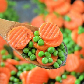 A wooden spoon holds sautéed sliced carrots and green peas over a pan of vibrant vegetables—perfect for anyone curious about how to cook frozen peas and carrots to perfection.