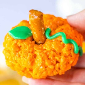 Orange Rice Krispie treat shaped like a pumpkin, complete with a pretzel stick stem and green icing leaf and vine, makes for the perfect Halloween delight.