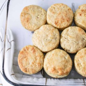 Biscuits, crafted with the classic Hardees Biscuits Recipe, are neatly arranged in a baking dish, resting on a white towel adorned with brown grid lines.