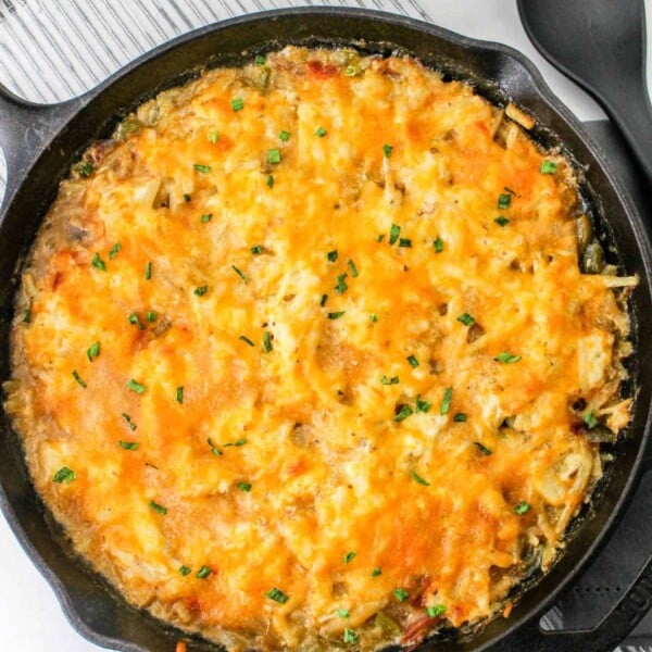 Hash brown casserole without soup in a cast iron skillet rests on a striped placemat, with a black serving spoon nearby.