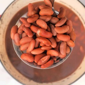 A ladle holds red kidney beans above a simmering pot of bean soup, perfect for those learning how to cook kidney beans on the stove.