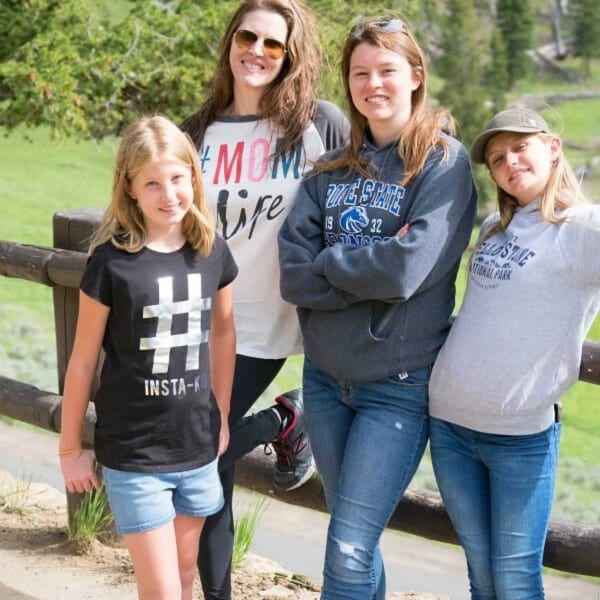 Four people posing casually outdoors by a wooden fence with lush greenery in the background, perhaps discussing how to start homeschooling.