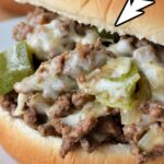 A close-up of a Sloppy Joe Philly Cheesesteak. The sandwich features ground meat mixed with peppers and onions, topped with melted cheese and served on a hamburger bun. A white arrow points to the filling, highlighting the ingredients. Text above reads "Philly Cheesesteak Sloppy Joes.