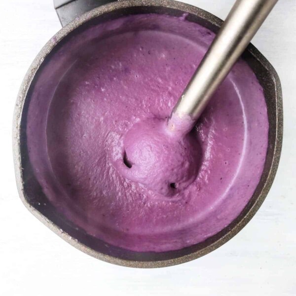 A blender effortlessly transforms ingredients into a vibrant purple pureed soup, swirling smoothly in the pot on a light surface.