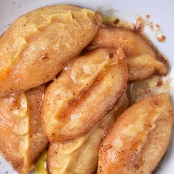 A plate with six golden-brown sweet potato dumplings rests on a pristine white surface.