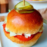 Crispy chicken sandwich made with frozen chicken patties in air fryer, topped with lettuce, tomato, and pickles on a bun, served on a white plate.