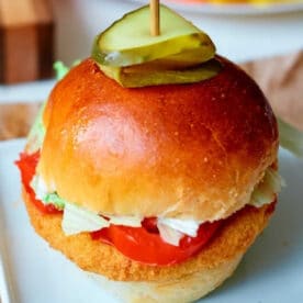 Crispy chicken sandwich made with frozen chicken patties in air fryer, topped with lettuce, tomato, and pickles on a bun, served on a white plate.
