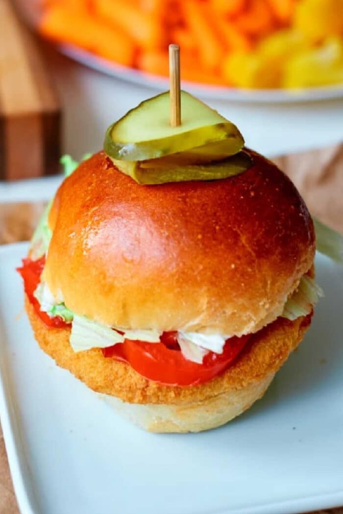 Crispy chicken sandwich made with frozen chicken patties in air fryer, topped with lettuce, tomato, and pickles on a bun, served on a white plate.
