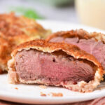 Close-up of a sliced venison cube steak, revealing tender pink wrapped in flaky pastry