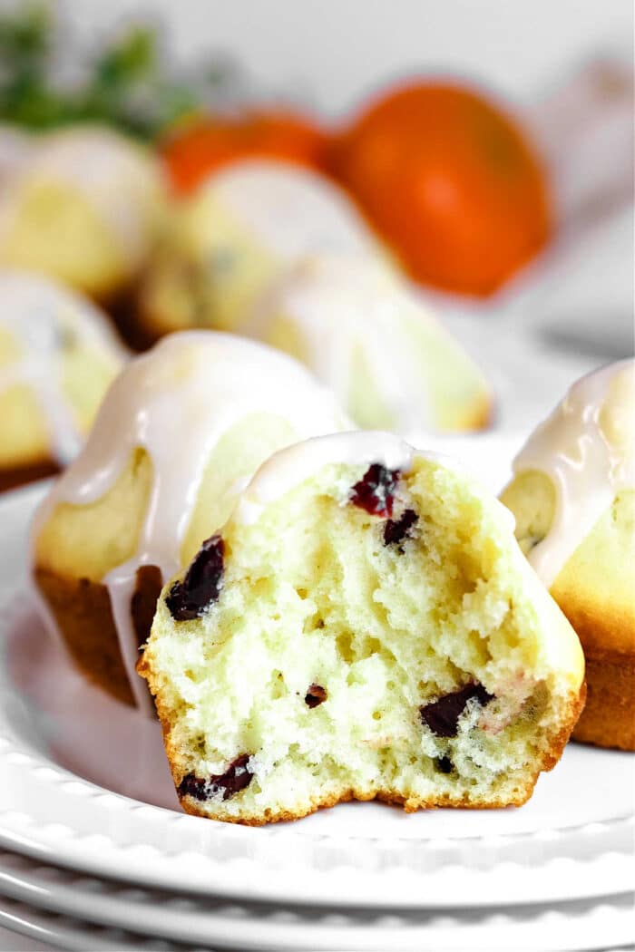 A sliced, healthy cranberry muffin with yogurt and icing sits on a plate, while more muffins and fresh oranges create an inviting background.