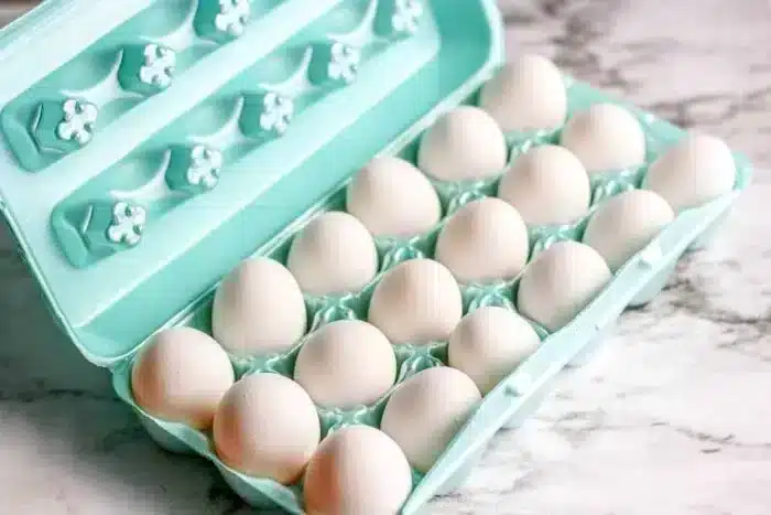 A light blue carton containing eighteen white eggs is open on a marble surface. The eggs are neatly arranged in two rows in their designated slots, 