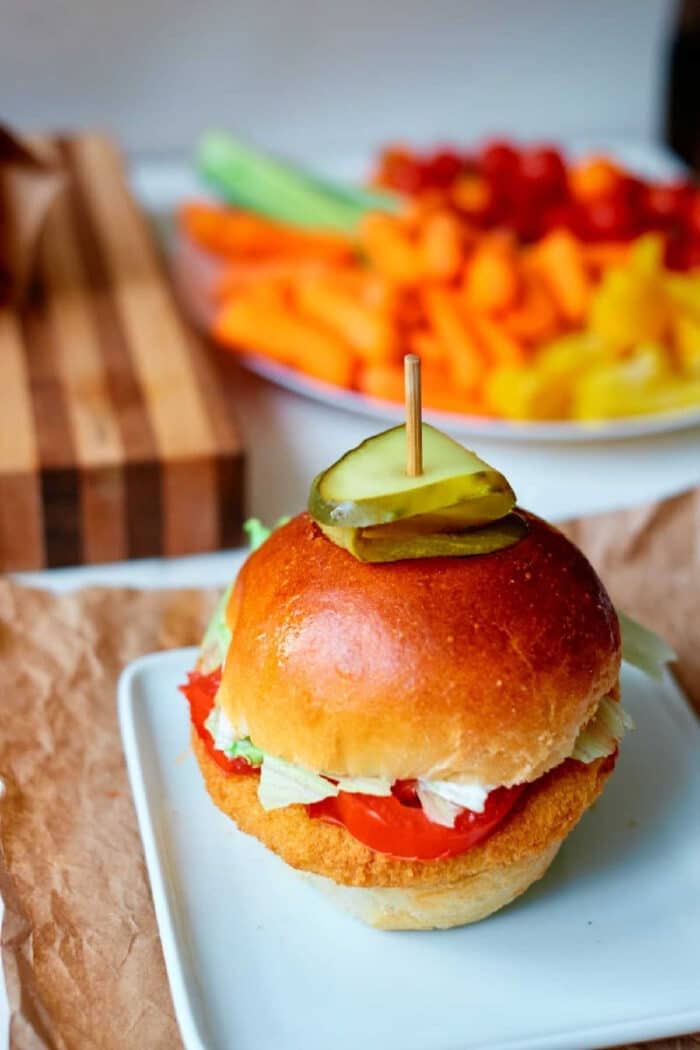 A chicken sandwich made with crispy frozen chicken patties in air fryer, topped with lettuce, tomato, and pickles on a bun, served on a white plate.