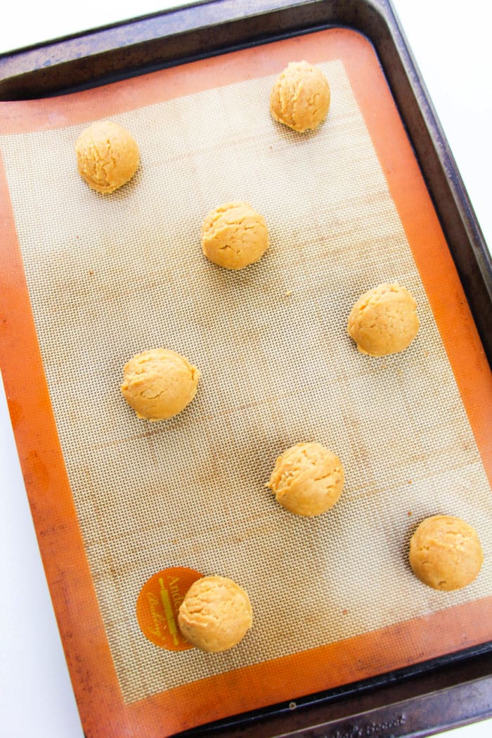 Eight of the best ever peanut butter cookies, in dough form, rest patiently on a baking tray lined with a silicone mat.