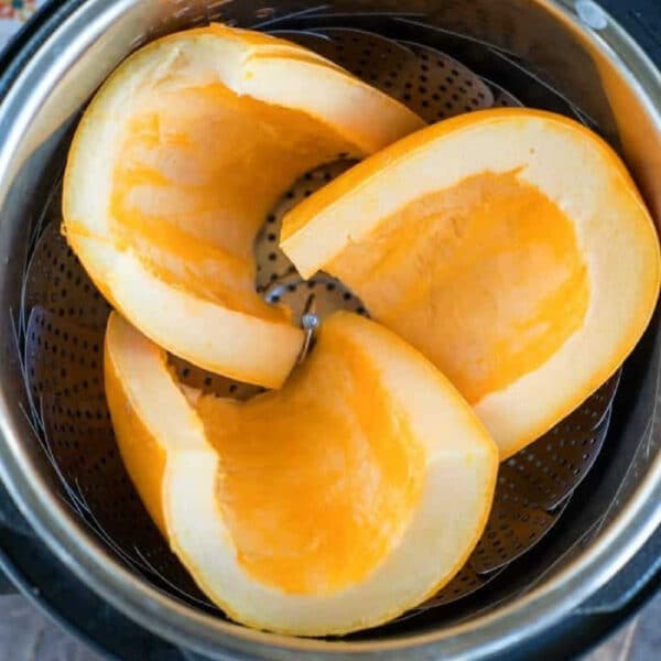 Three raw pumpkin wedges in a steamer basket inside a pressure cooker, ready to become perfectly tender pressure cooker pumpkin on a wooden surface.