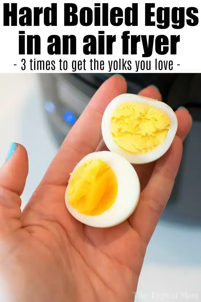 A hand is holding two halves of a hard-boiled egg in front of an air fryer. The egg on the right has a fully cooked yolk, while the egg on the left has a slightly soft, partially cooked yolk. The text above reads, "Air fryer hard boiled eggs - 3 times to get the yolks you love -".