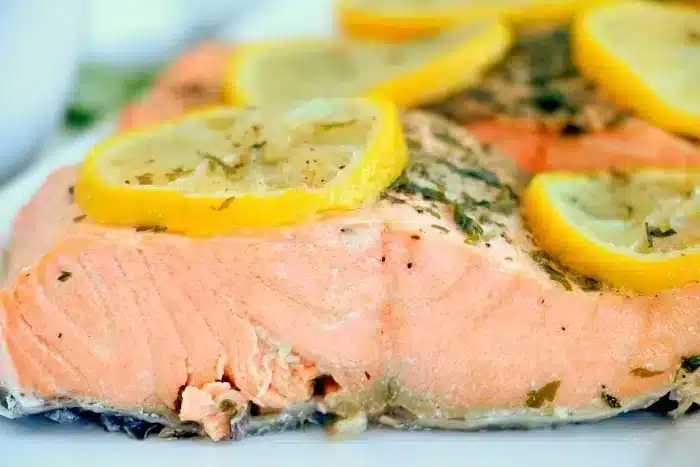 Close-up of the best baked salmon fillet, adorned with lemon slices and herbs. The pink flesh of the salmon is visible, and the lemon pieces are evenly placed on top, accentuating the dish's seasoning and presentation.